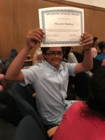 Hussein holding a certificate awarded for high achievement.