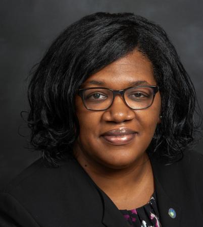 woman with glasses wearing a blazer against a grey background