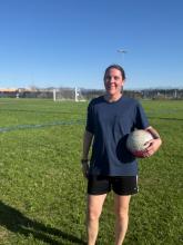 Melissa poses with a soccer ball on a field.
