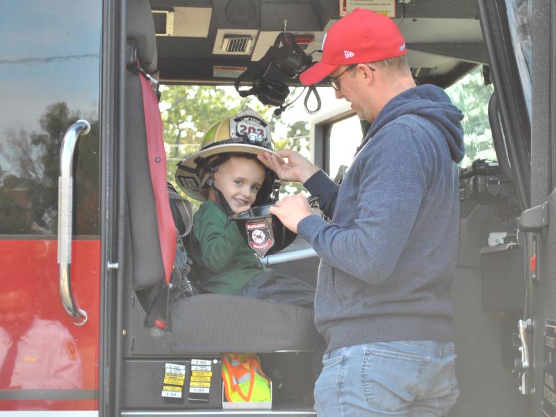 A father and son sit in a fire engine and try on a firefighter helmet while visiting Station 203 during an open house event in 2019.